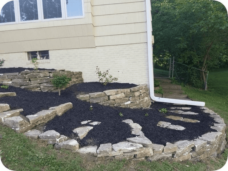 Freshly landscaped garden bed with black mulch and stone edging beside a house