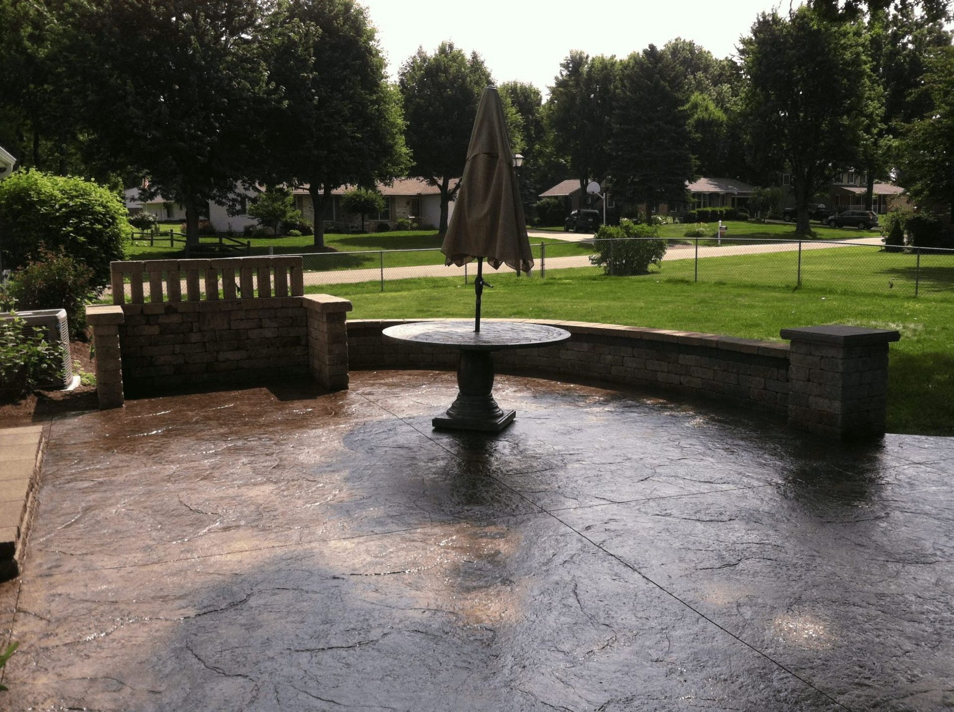 Patio with a central umbrella table, stone benches, and a park lawn and trees in the background