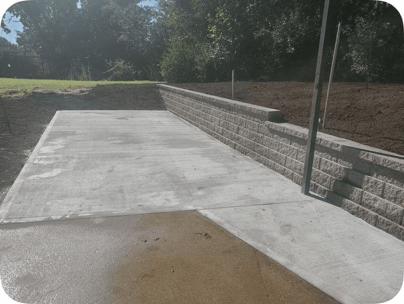 Concrete accessibility ramp with retaining wall and metal handrail beside a grassy area.
