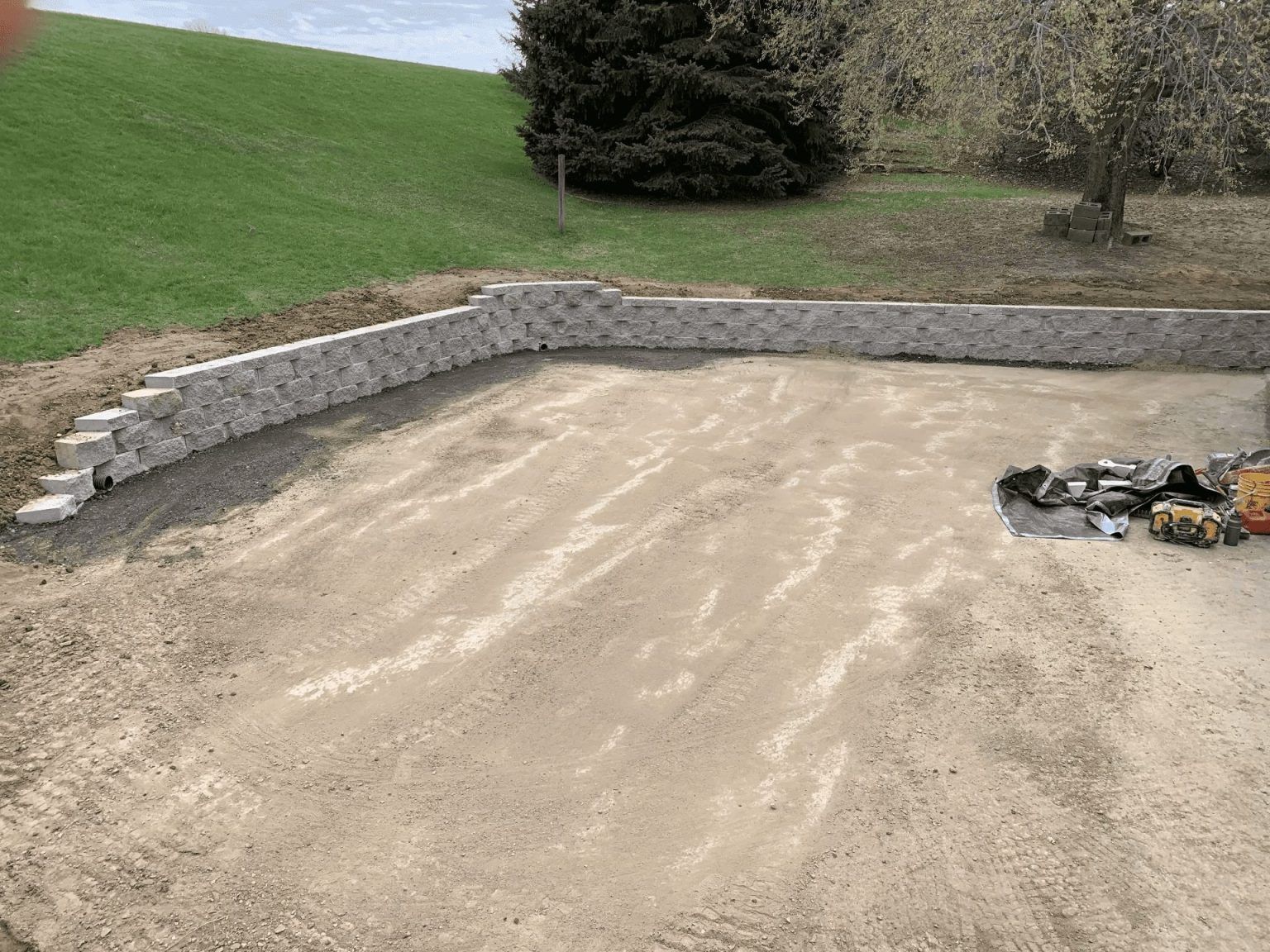 Gravel driveway base with stone retaining wall beside a grassy slope and trees