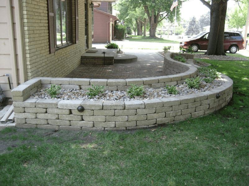 Curved brick planter edging a house patio with sparse plants and a grassy lawn