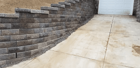 Concrete driveway beside a gray stone retaining wall leading to a white garage door