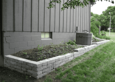 Gray building with a raised stone planter bed and grass beside it