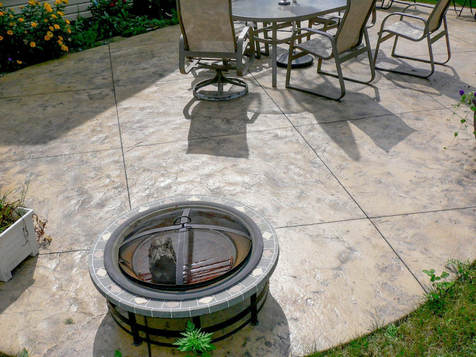 Backyard patio with stone paving, outdoor chairs, and a circular fire pit in the foreground