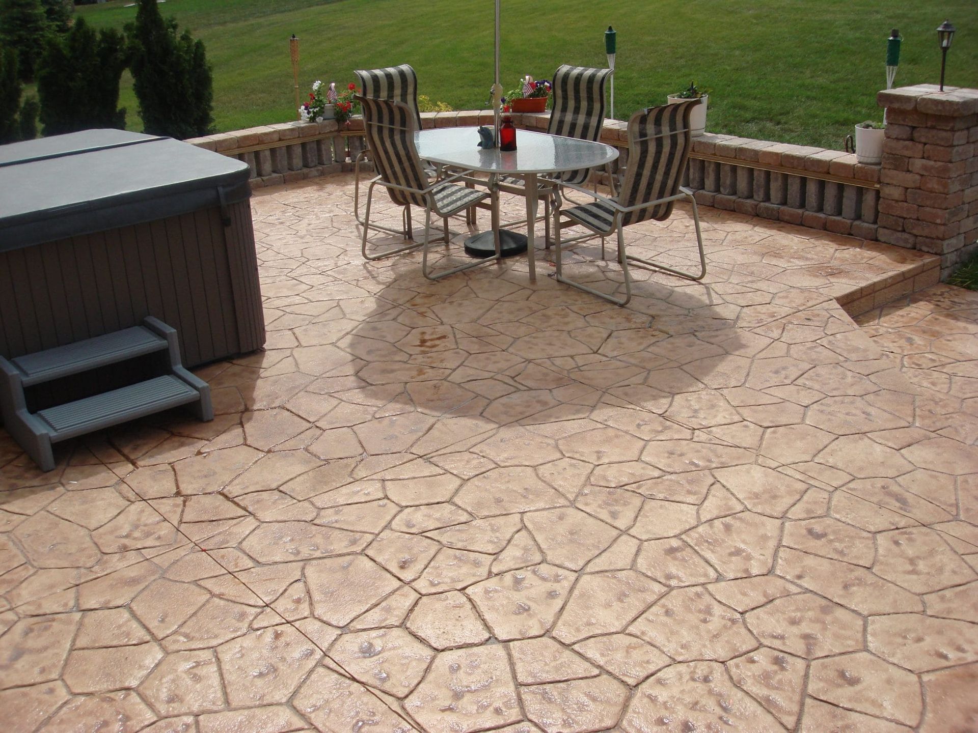 Patio with stone paving, metal table and chairs, grill, and brick wall overlooking a grassy yard