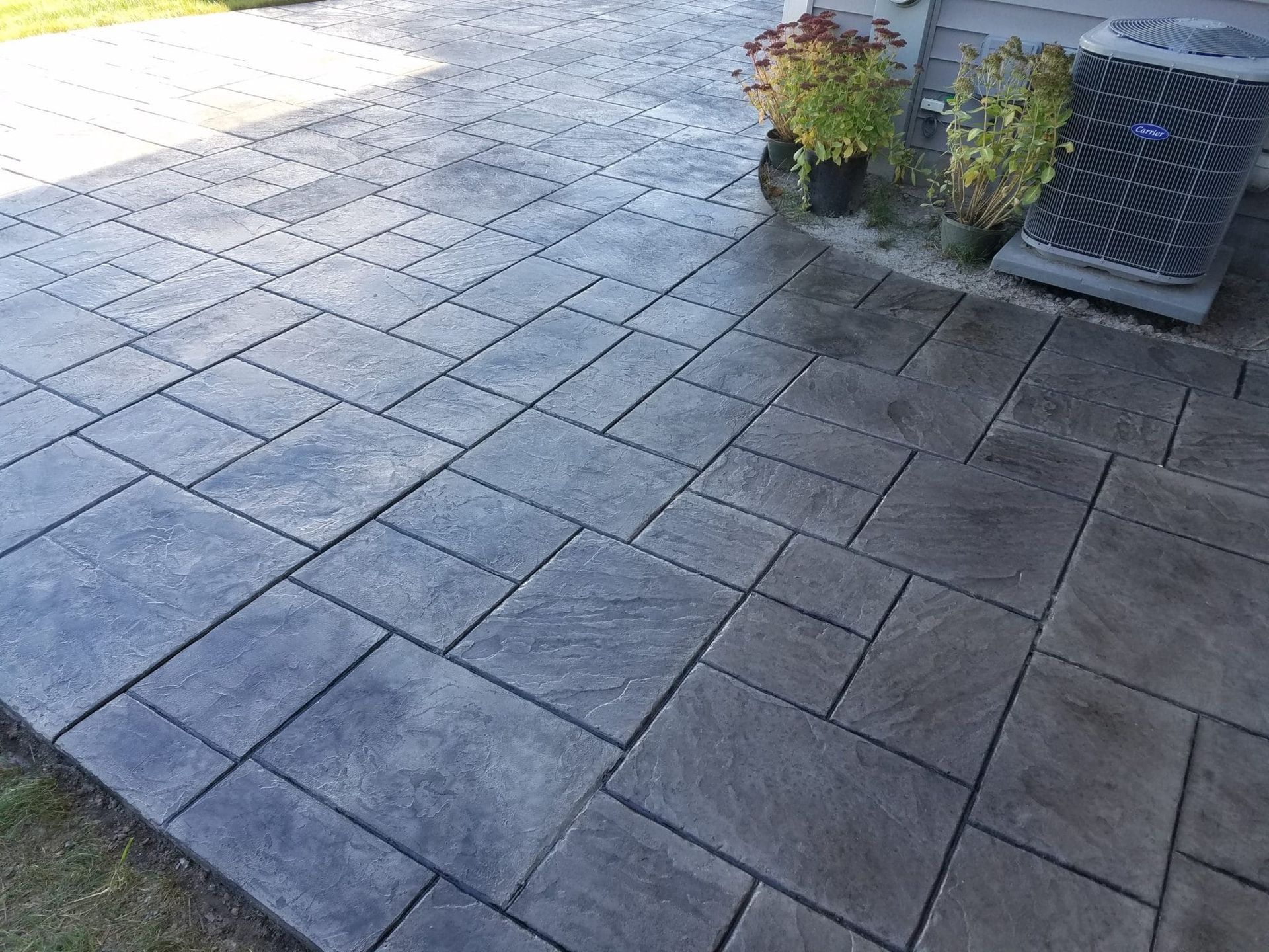 Stone patio with dark square pavers, a planter of red flowers, and an outdoor vent or unit on the right.