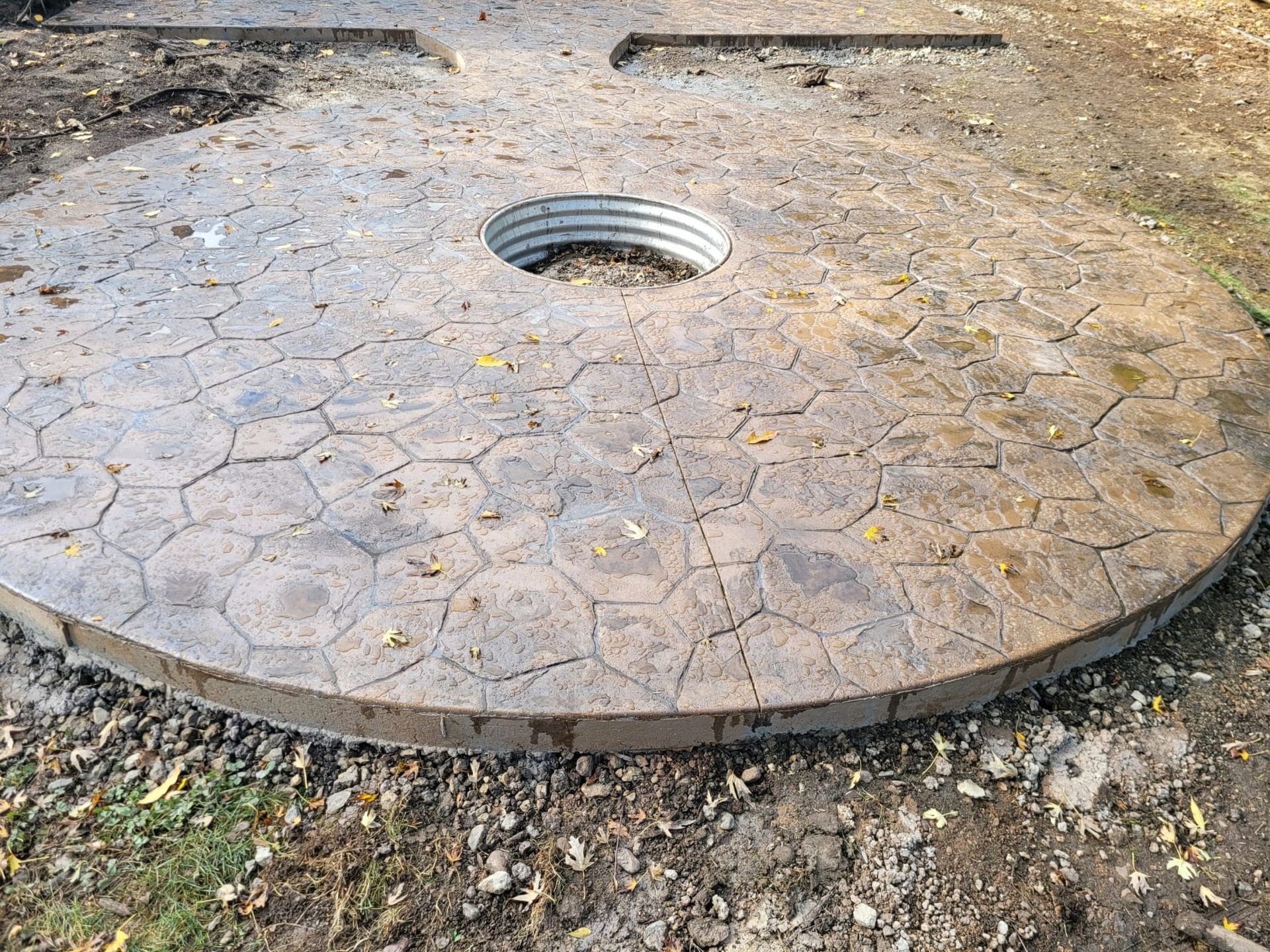 Circular stone platform with a central manhole cover embedded in a gravel outdoor area