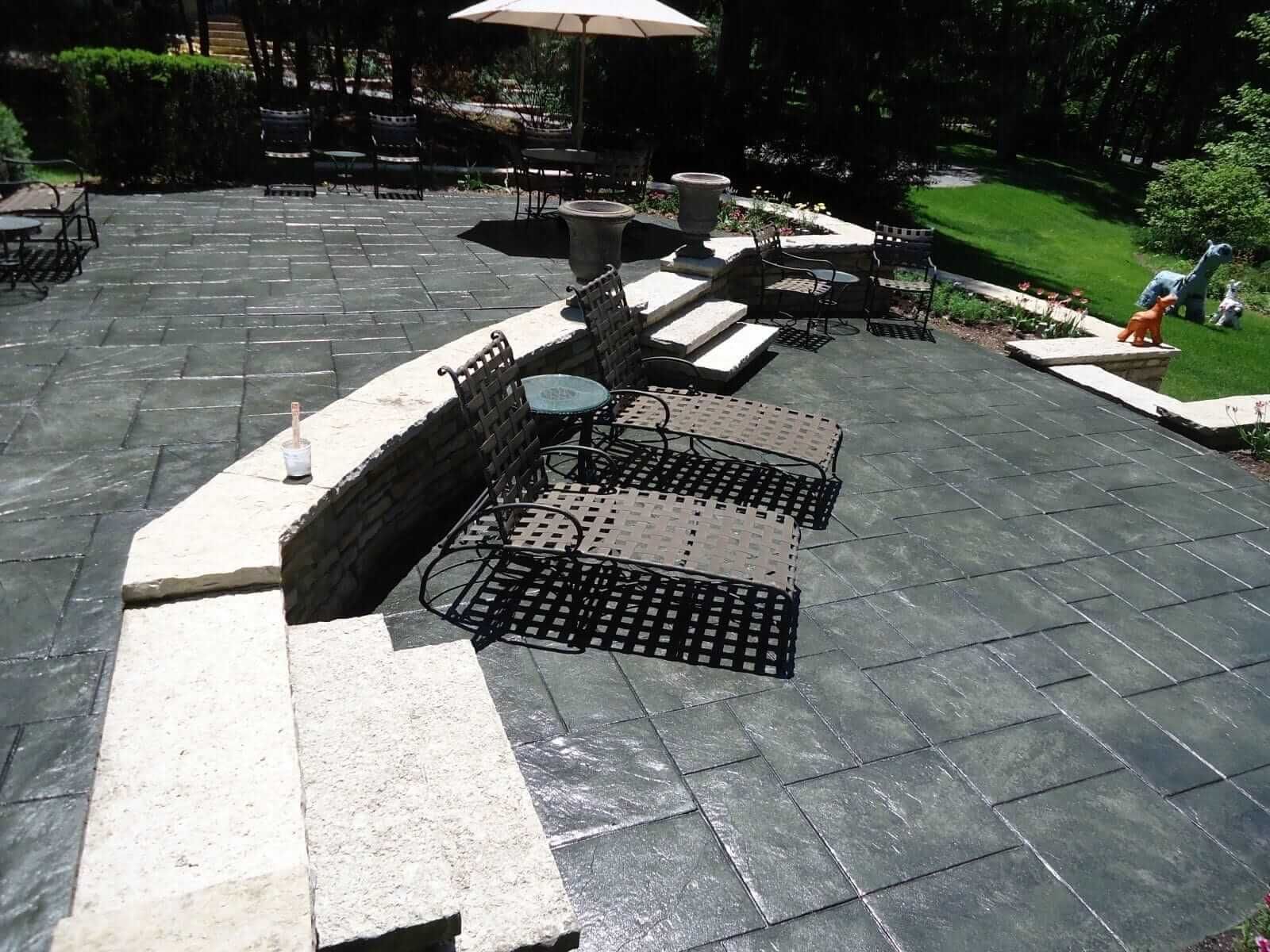 Stone patio with curved retaining wall, two chairs, and lawn in a backyard garden.