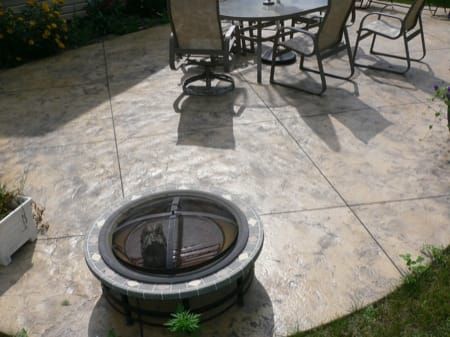 Patio with stone paving, outdoor table and chairs, and a round fire pit in the foreground