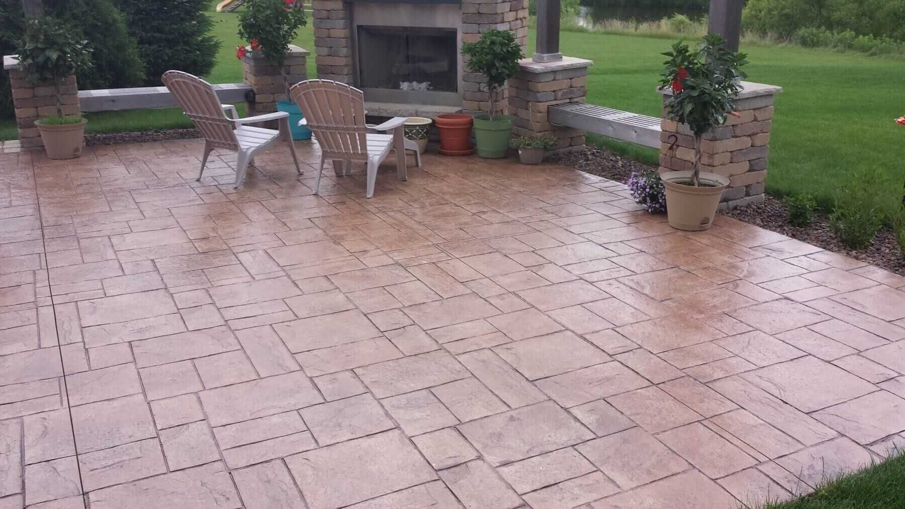 Rainy patio with wet brick pavers, two chairs, and potted plants beside a grassy yard