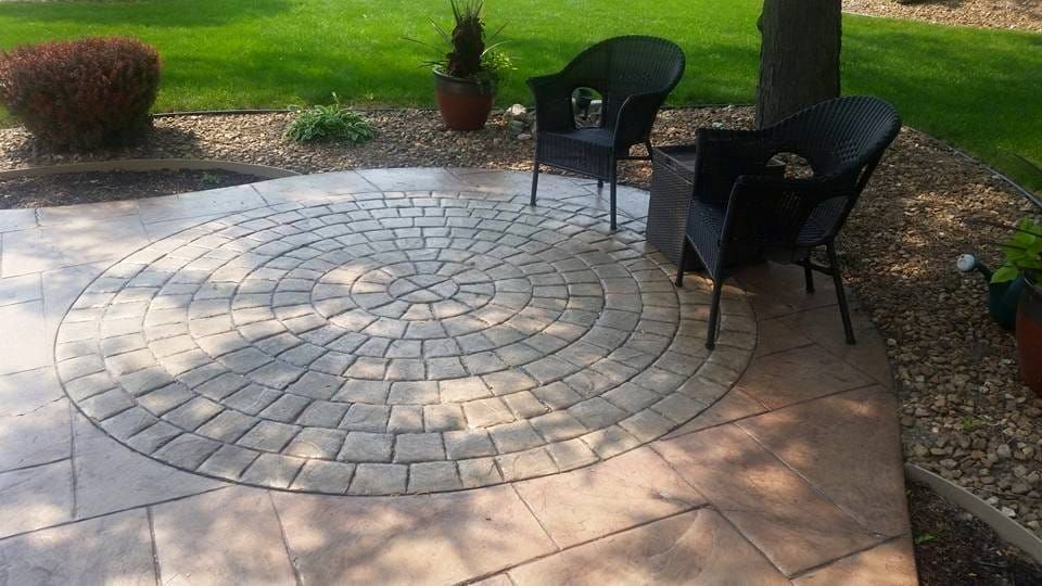 Circular stone patio with two black chairs and a small table in a garden