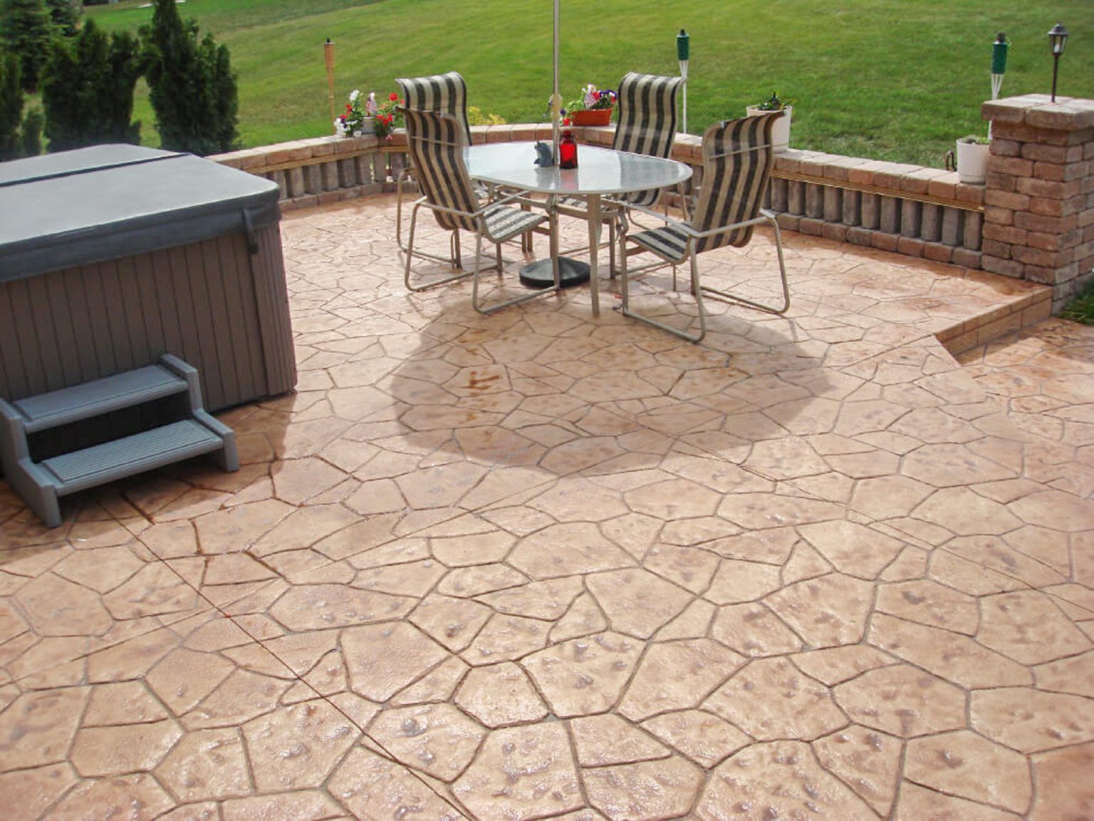 Patio with stone flooring, outdoor dining table and chairs, and a hot tub beside a grassy yard