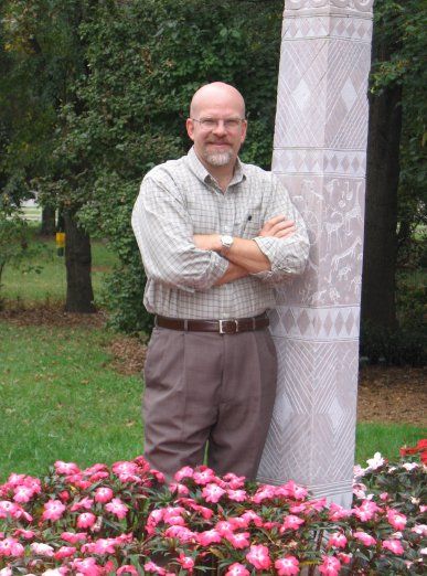 a man with his arms crossed is standing next to a statue in a park .