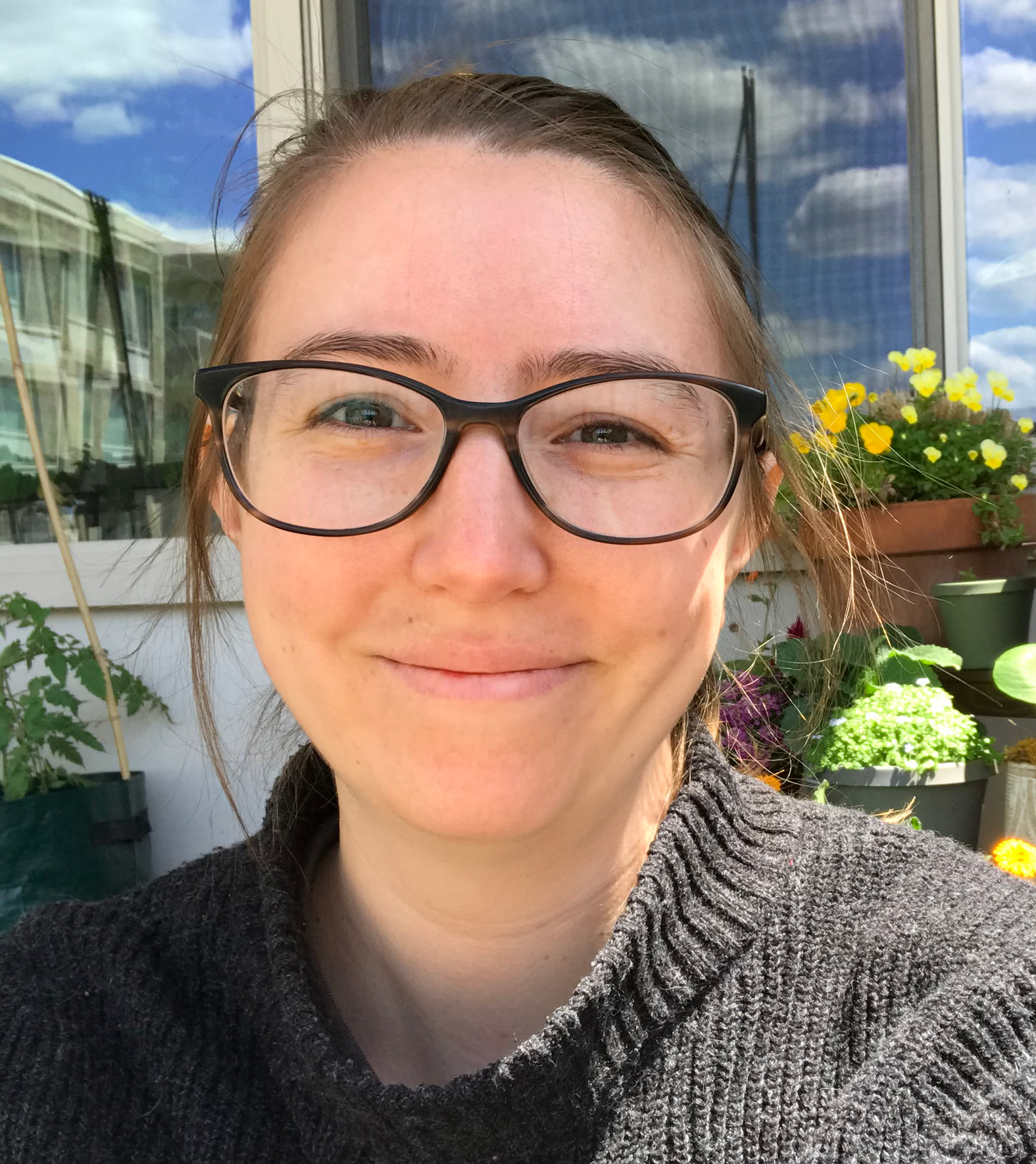 A woman wearing glasses and a sweater is smiling for the camera.