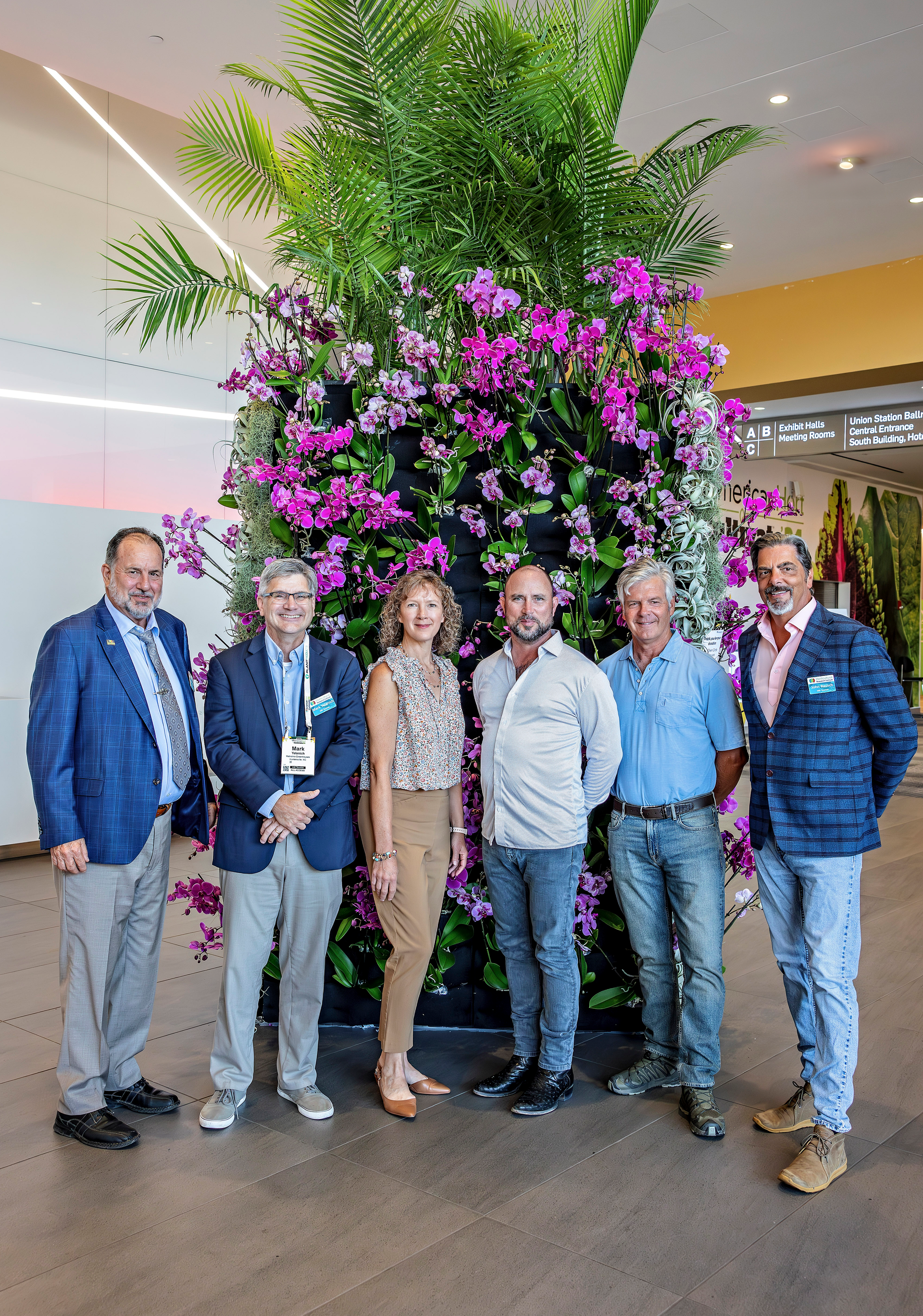 A group of people are standing in front of a wall of flowers.