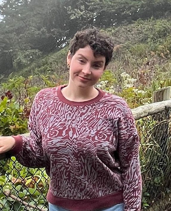 A woman in a sweater is standing next to a chain link fence.