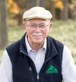 A man wearing a hat and a vest is smiling for the camera.