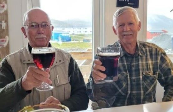 Two older men are sitting at a table holding glasses of beer.