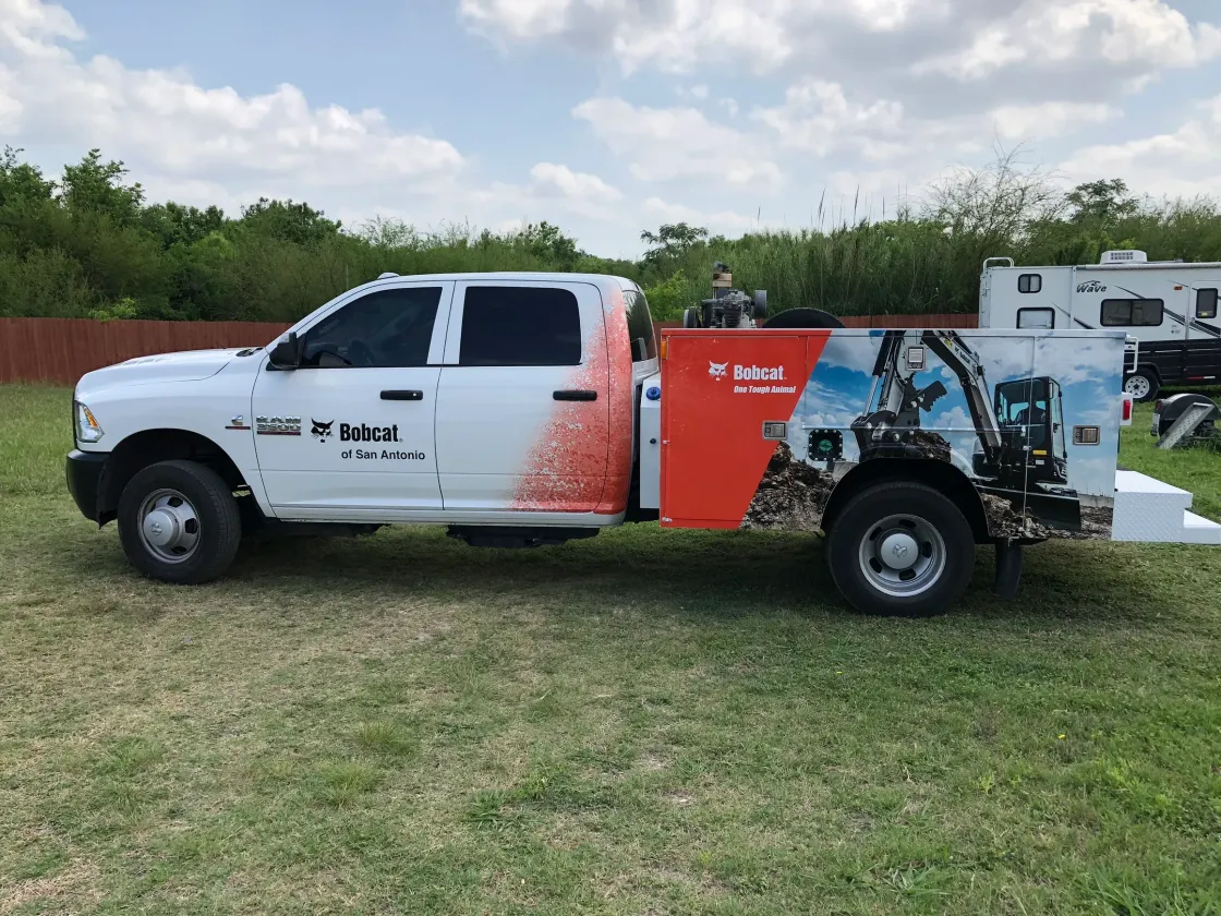 A white truck with a bobcat logo on the side is parked in a grassy field.