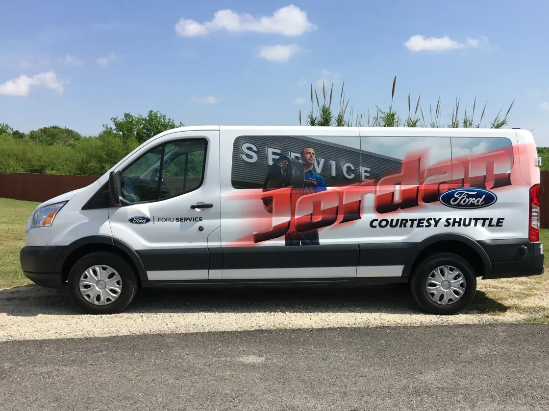 A white van with a ford logo on the side is parked on the side of the road.