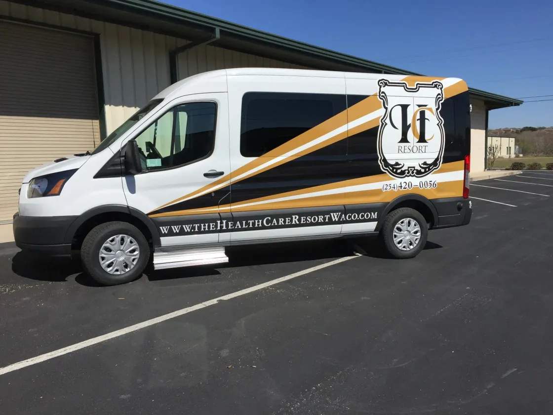 A white van is parked in a parking lot in front of a building.