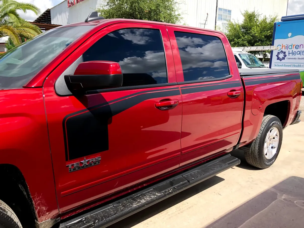 A red truck with black stripes on the side is parked in a parking lot.