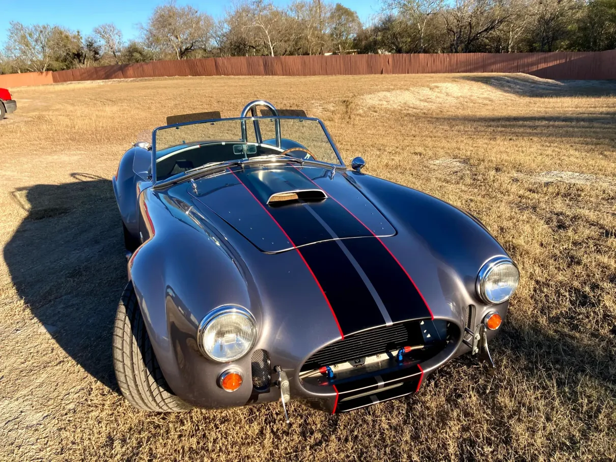 A silver sports car with black and red stripes is parked in a field