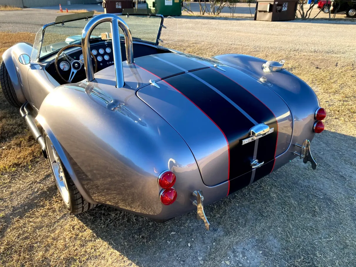 A silver sports car with black stripes is parked in a dirt lot