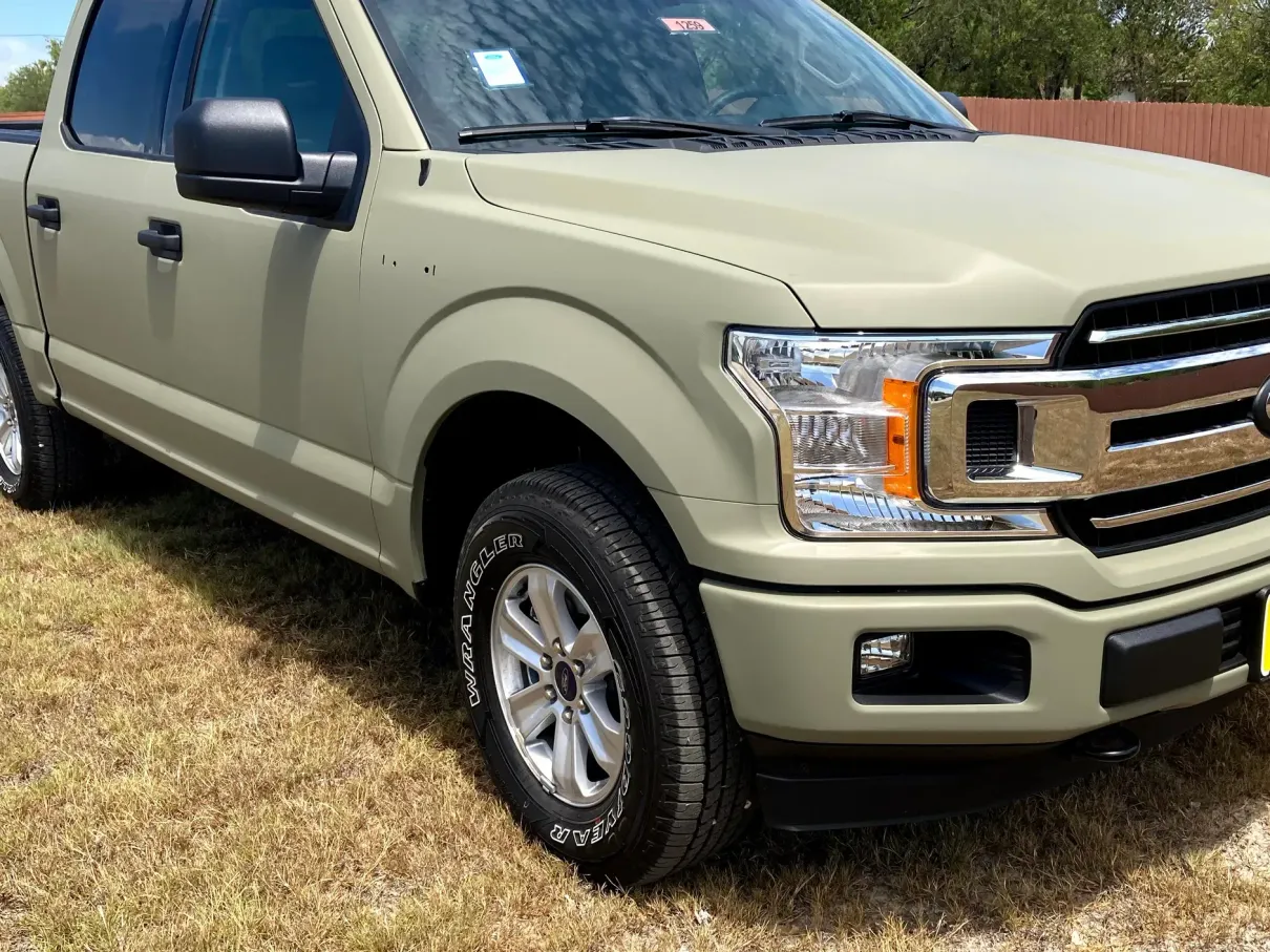 A green ford f150 truck is parked in the grass.