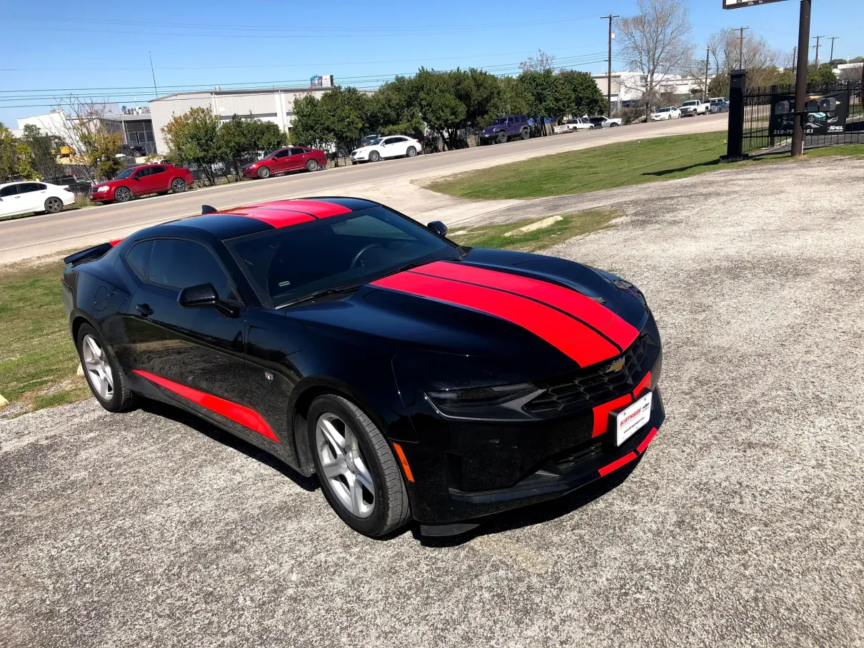 A black car with red stripes on the side is parked on the side of the road.