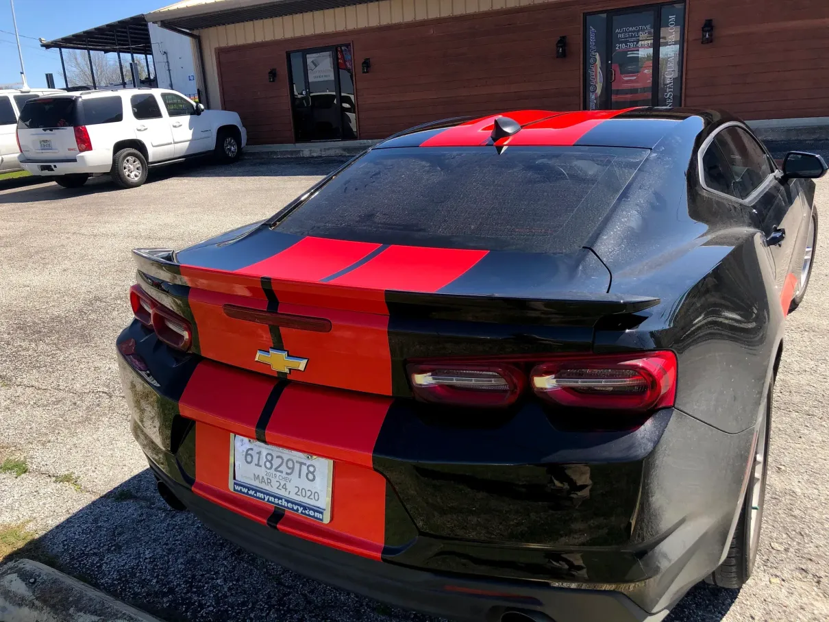 A black car with red stripes is parked in front of a building