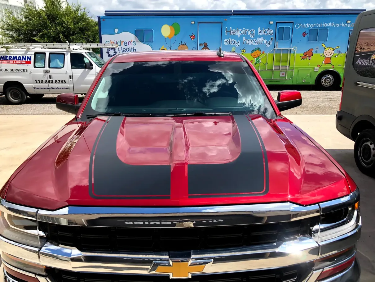 A red truck with black stripes on the hood is parked in a parking lot.