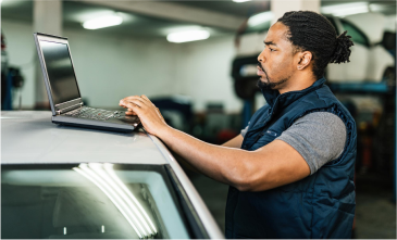 A man is using a laptop computer on top of a car.