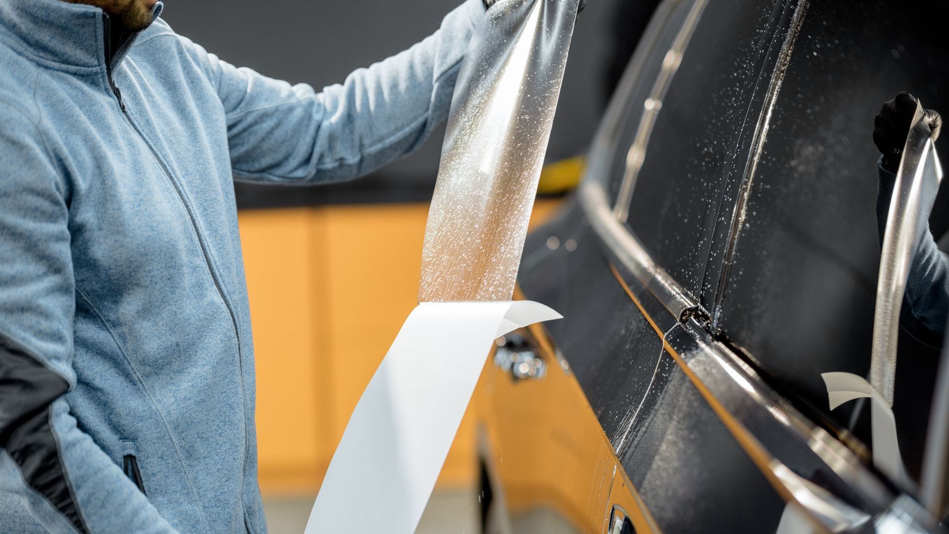 A man is wrapping a car with a piece of paper.