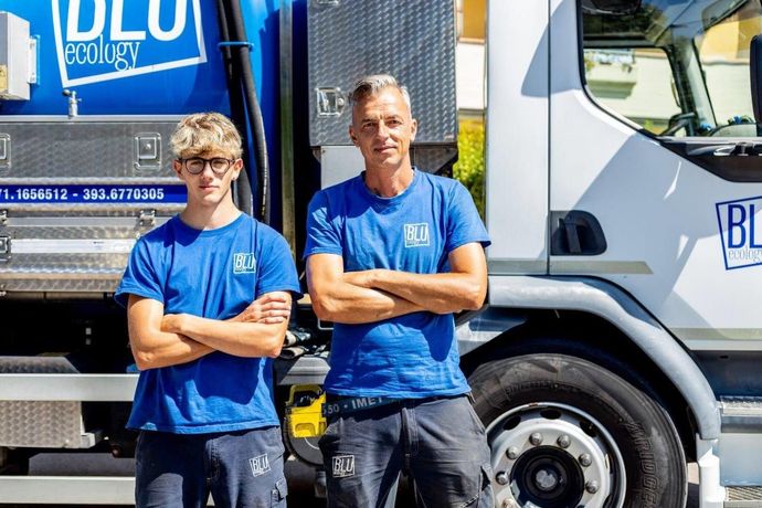 Due uomini con le camicie blu sono in piedi con le braccia incrociate davanti a un camion blu.