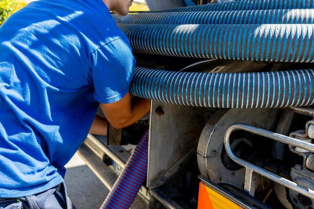 Uomo con camicia blu che collega i tubi a un camion, probabilmente per il pompaggio.