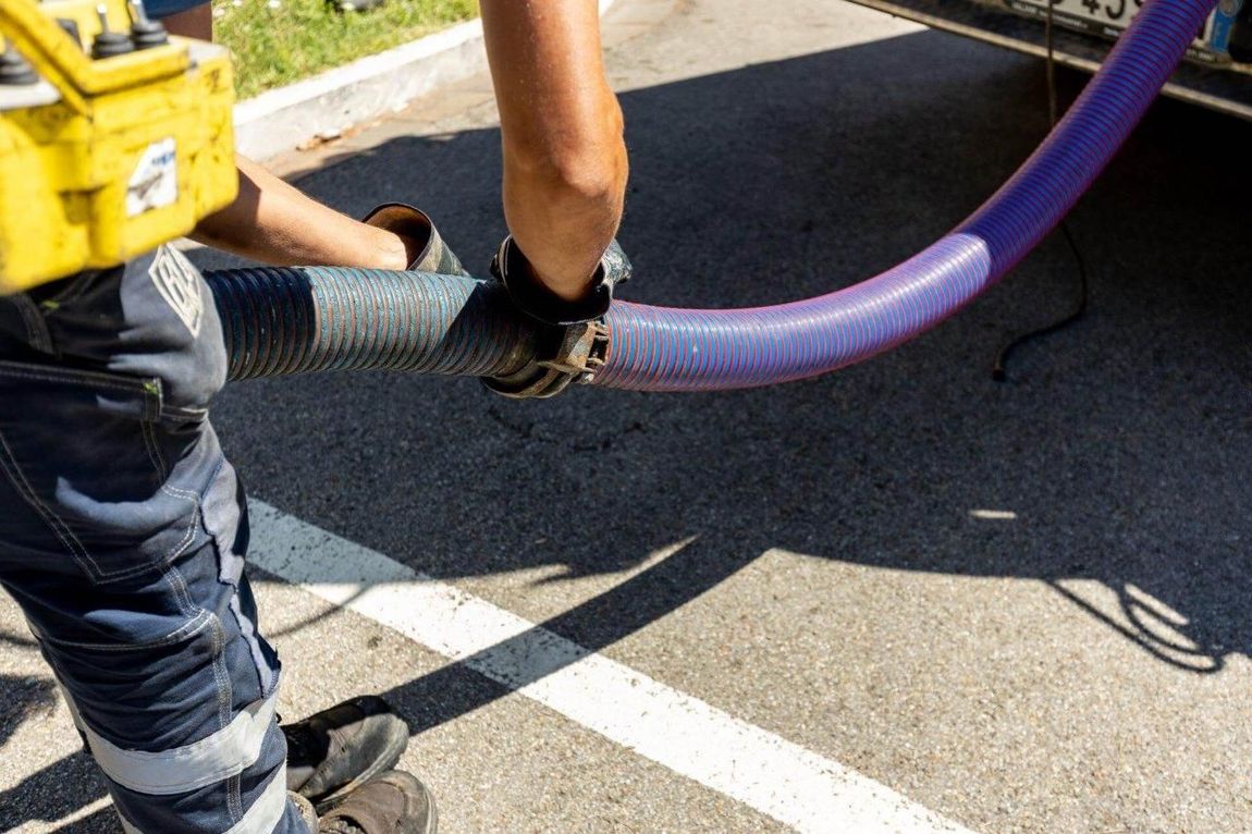 Persona che collega un tubo viola a un veicolo, probabilmente per un intervento di manutenzione, all'aperto.