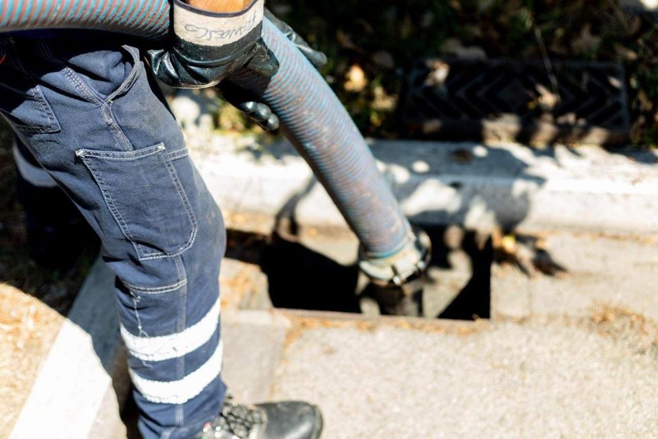 Un operaio in blue jeans e guanti pulisce uno scarico con un tubo.