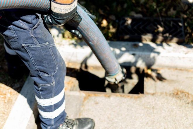 Un operaio in blue jeans e guanti pulisce uno scarico con un tubo.