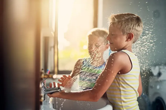 Due bambini schizzano acqua in un bagno, uno dei quali viene spruzzato con l'acqua.