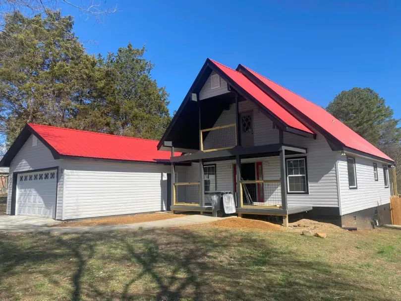 A-frame house and attached garage with red metal roofs, gray siding, and a wooden porch under construction.