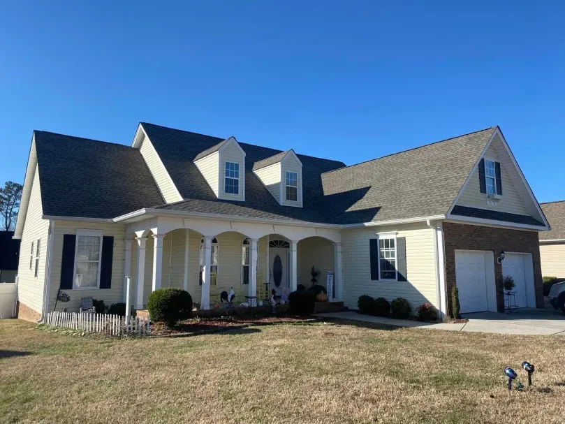 Yellow house with gray roof, white columns, blue sky. Garage on right.