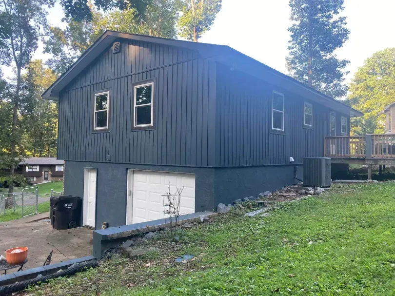 Blue house with white garage doors and windows, set in a grassy yard.