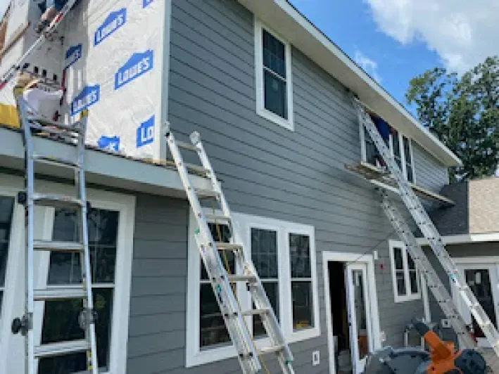 House exterior under construction, gray siding being installed, ladders, windows.