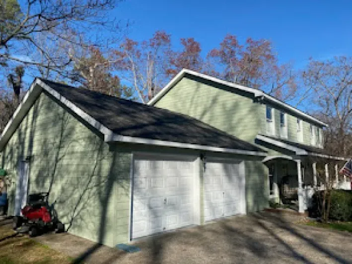 Green house with attached garage, two garage doors, dark roof, sunny day.