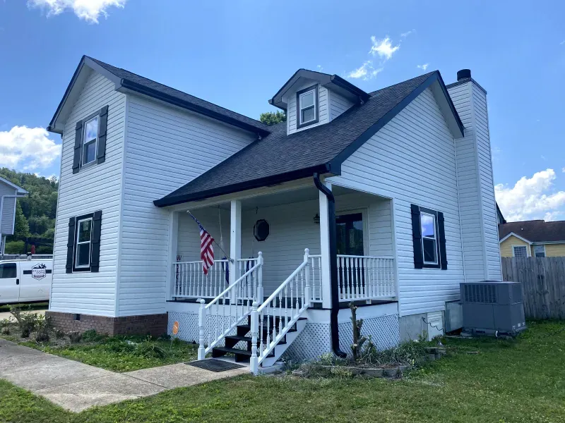 White two-story house with black trim, porch, and a US flag. Blue sky.