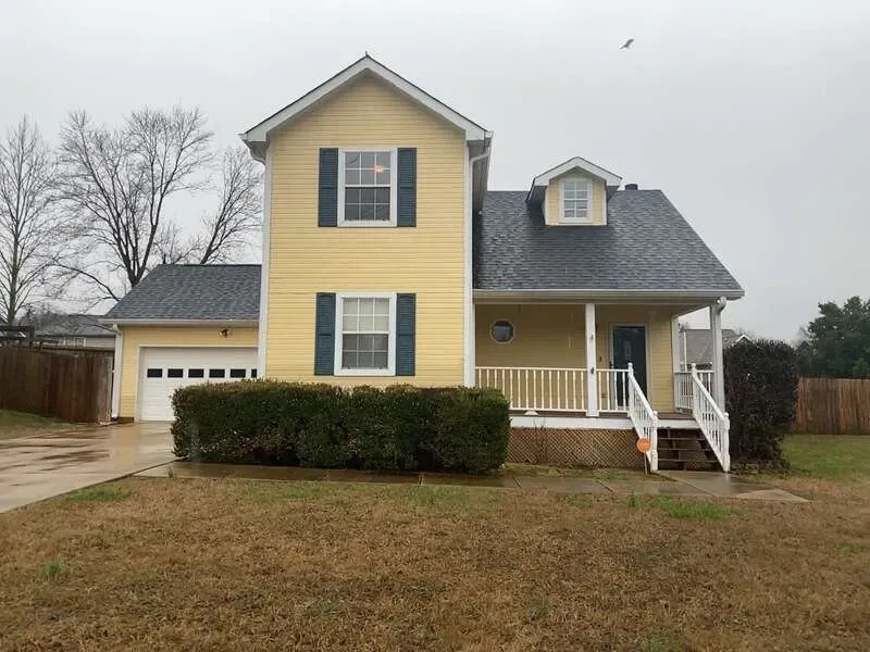 Yellow two-story house with black shutters, white porch, and attached garage on a cloudy day.