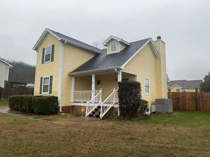Yellow house with dark roof and white trim under an overcast sky.