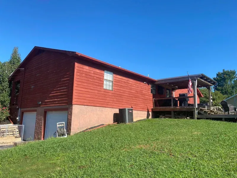 Red-sided house with a deck and a grassy yard under a blue sky; a garage door is visible.