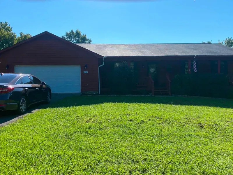 Red house with a white garage door and a car parked in front. Green grass and a blue sky.